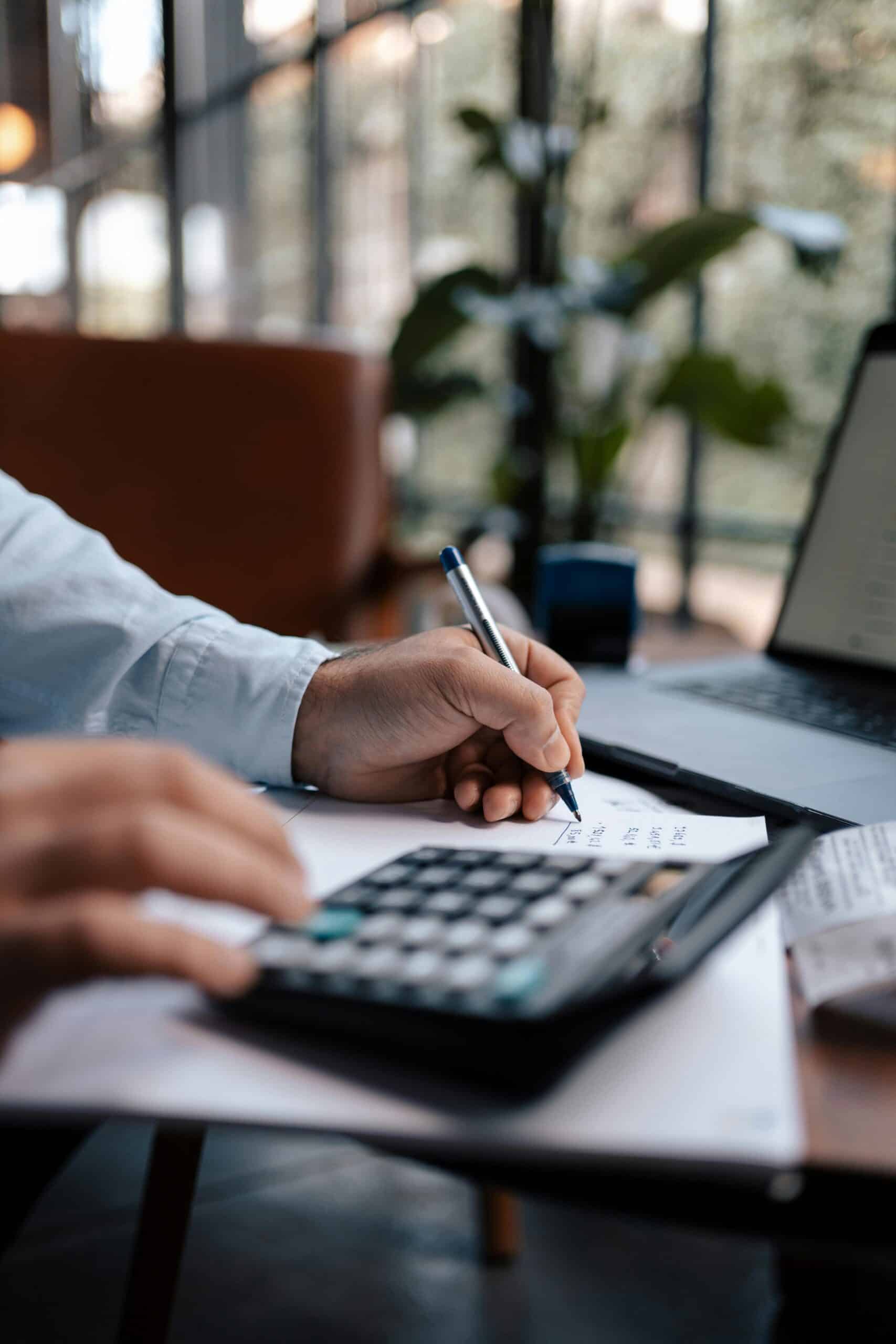 Free A person calculating finances with a calculator and pen on a desk indoors. Stock Photo